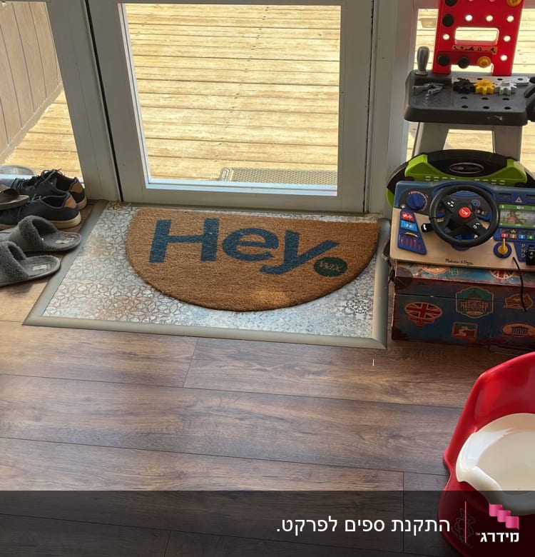 רצפת פרקט חומה ליד דלת זכוכית עם שטיחון "Hey".